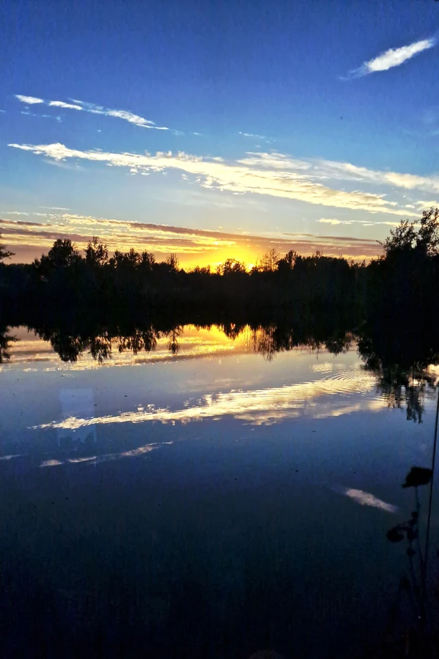 Goldener Sonnenuntergang über einem See unter blauem Himmel mit weißen Wolken