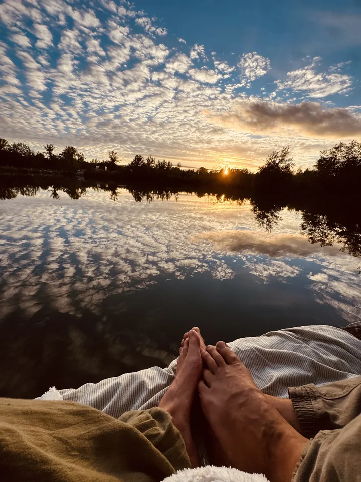 Blick von einer Decke über den See in den Sonnenuntergang, mit Füßen im Vordergrund