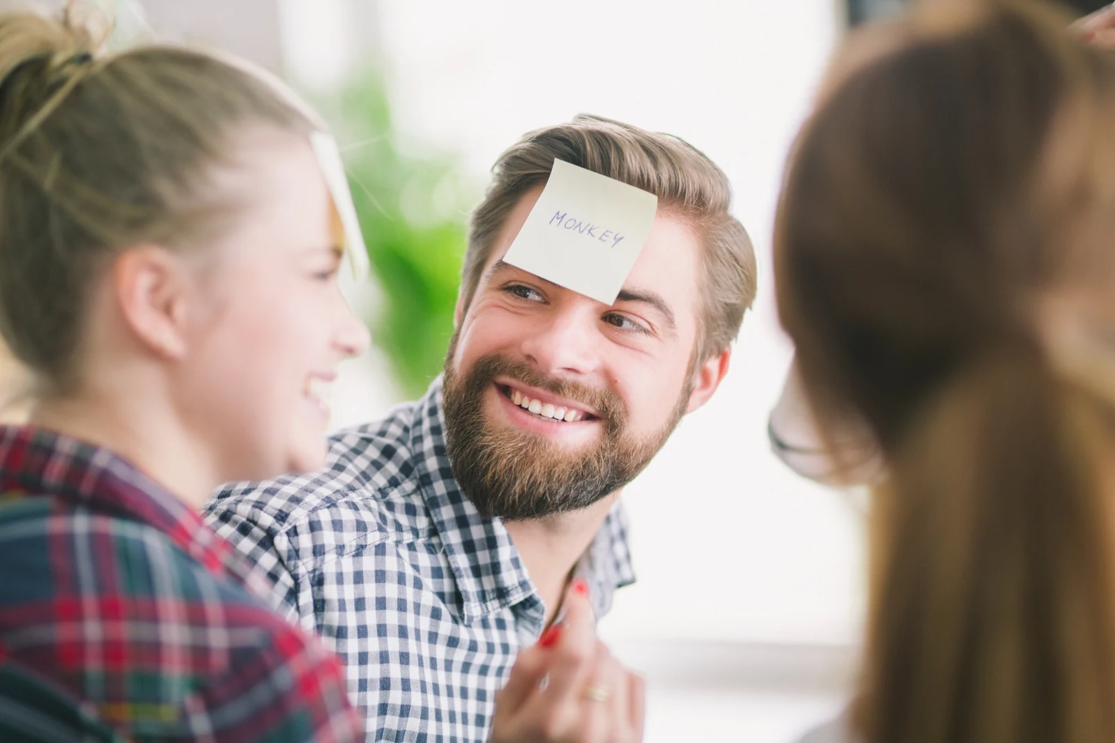 Ein lächelnder Mann mit dem Post-it „Monkey“ auf der Stirn im Gespräch mit zwei Frauen